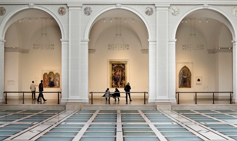 People view artwork along a hallway framed by three large arches in Brooklyn Museum’s Beaux-Arts Court.