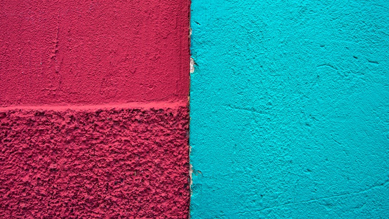 Meeting point of two colonial buildings' stucco exterior walls, one painted deep raspberry red and the other light blue