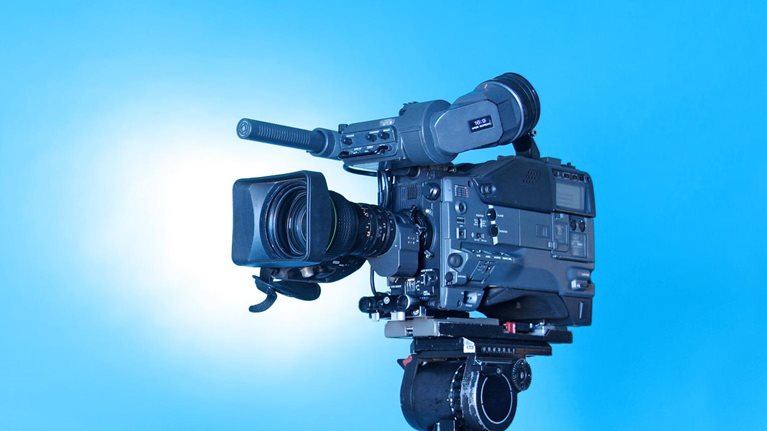A professional video camera on a tripod with a rich gradient blue background.